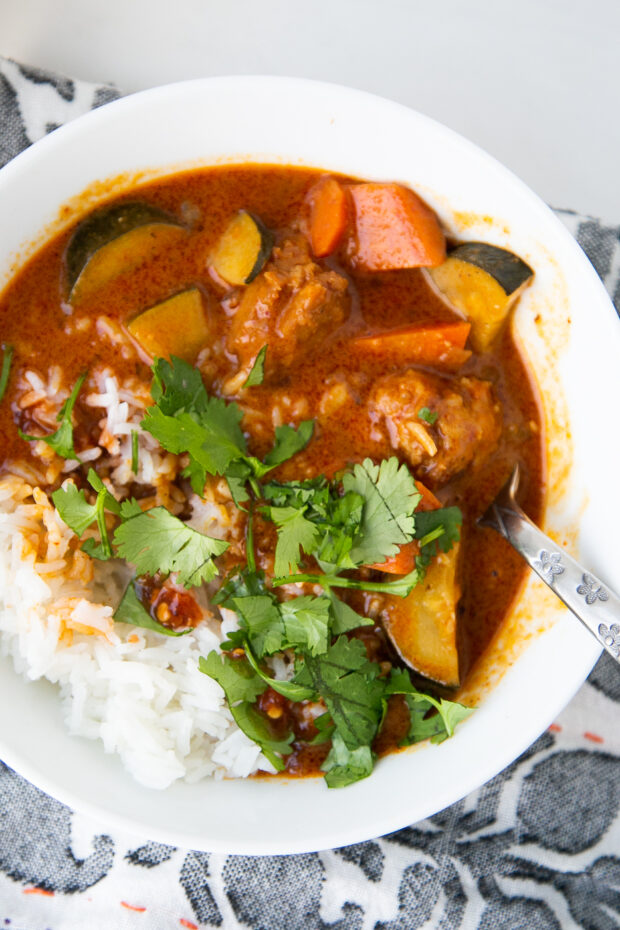 A white bowl of Thai chicken meatball curry with carrots and zucchini alongside some steamed jasmine rice and sprinkled with some fresh cilantro.