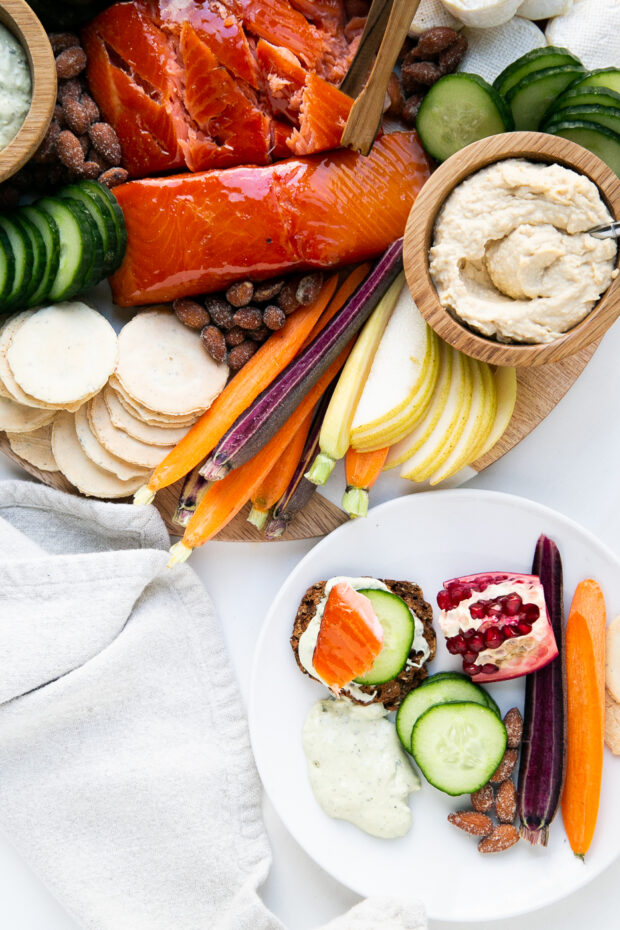 Smoked salmon platter with lots of things to eat around it, including sliced pears, rainbow carrot sticks, and hummus.