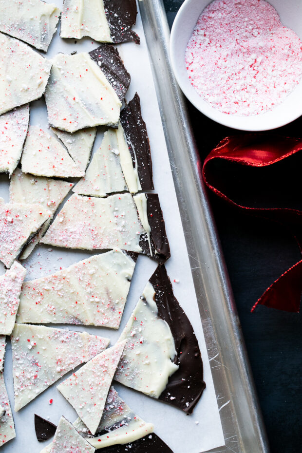 Another overhead view of broken peppermint bark with a red Christmas ribbon on the side near a bowl of crushed candy canes.