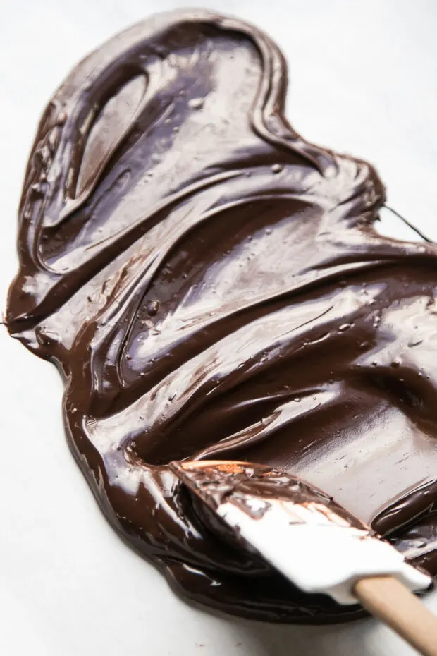 Melted dark chocolate being spread over parchment with a spatula.