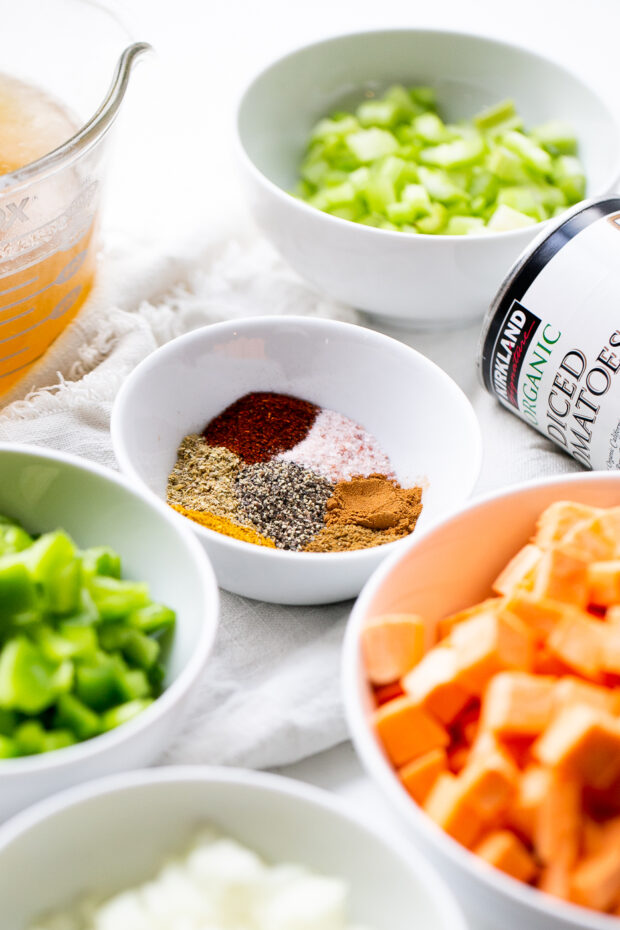 Some ingredients for Moroccan paleo turkey chili -- a small white bowl with spices, diced sweet potatoes, diced bell pepper, diced celery, chicken broth, diced tomatoes.