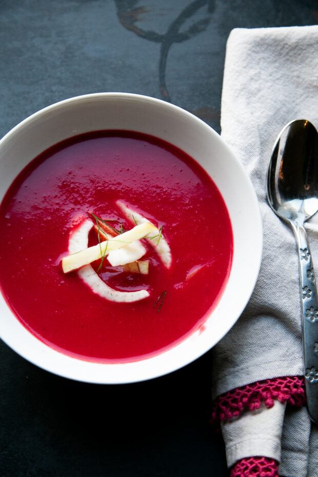 White bowl with bright pink pureed beet soup. Soup has an apple fennel slaw for garnish.