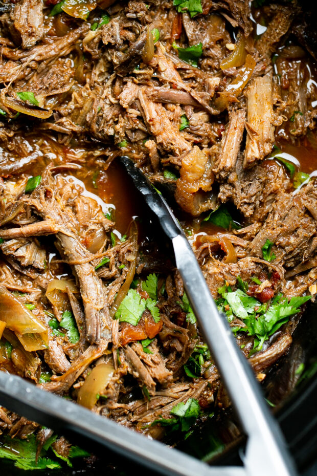 Close up of Chipotle Barbacoa Beef with a pair of tongs.