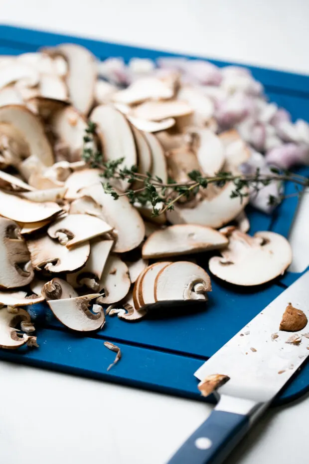Blue cutting board with sliced mushrooms and fresh thyme.