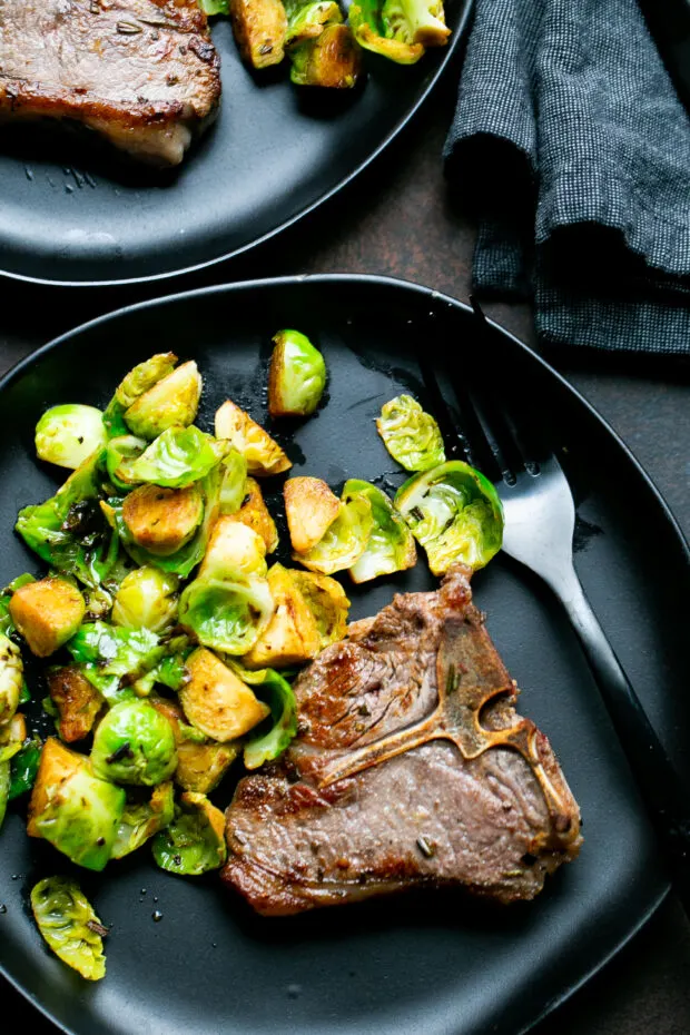 Sauteed Lamb Loin Chop on a black plate with a black fork alongside some Brussels sprouts.