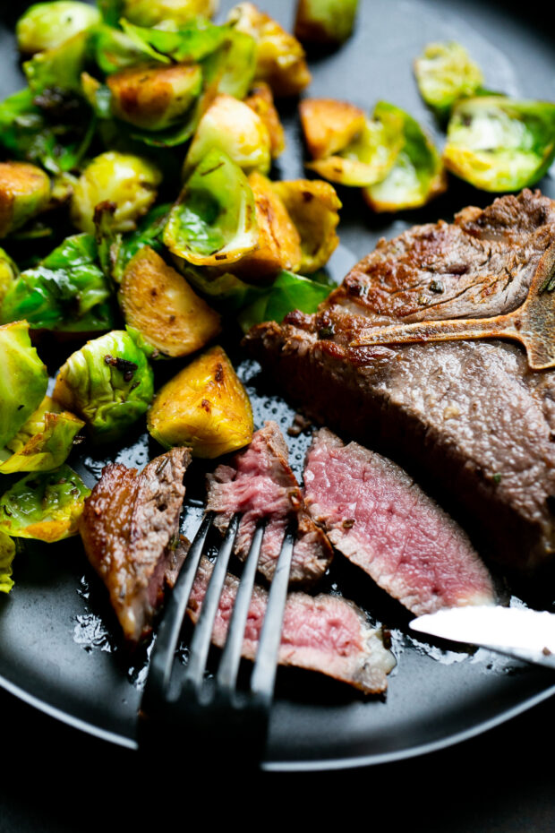Another shot of a sliced lamb loin chop with some cooked Brussels sprouts on a black plate.