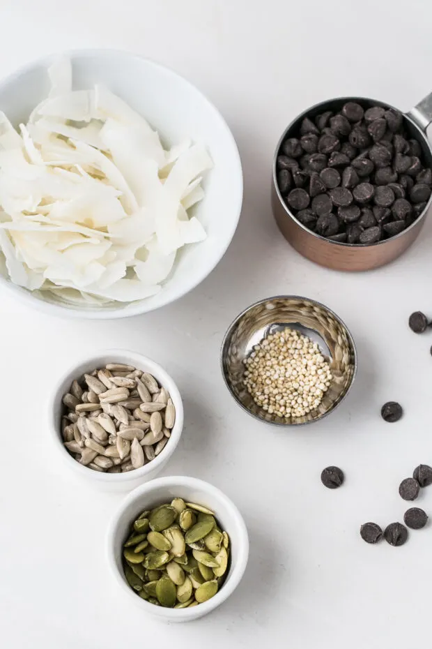 Bowls of ingredients -- coconut flakes, sunflower seeds, quinoa, pumpkin seeds, and chocolate chips.