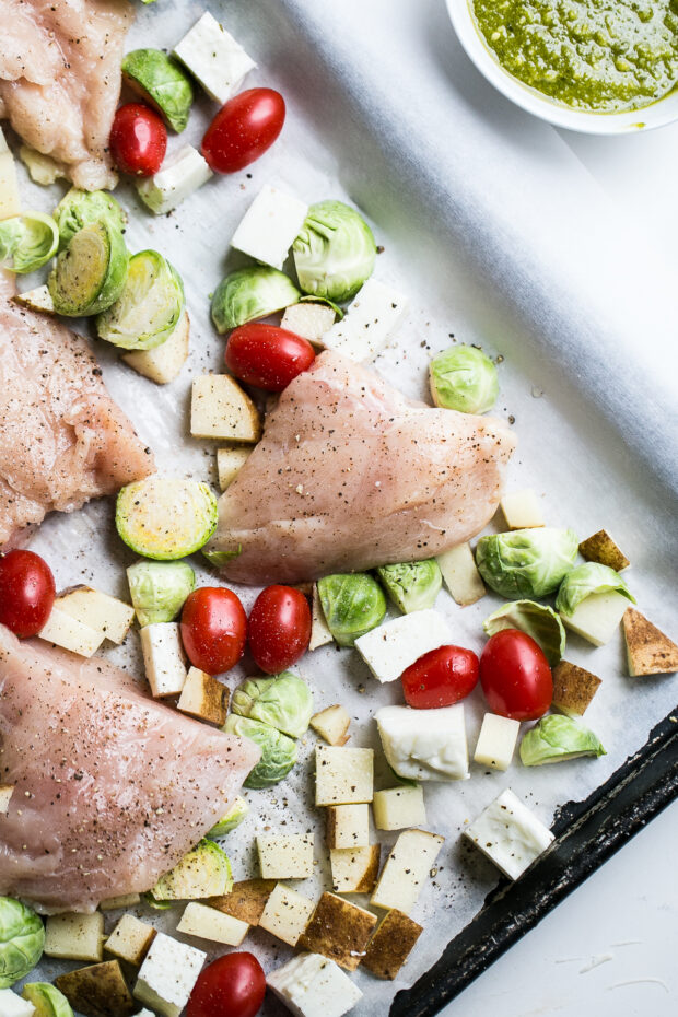 Chicken and vegetables on a parchment-lined sheet pan ready for the oven.