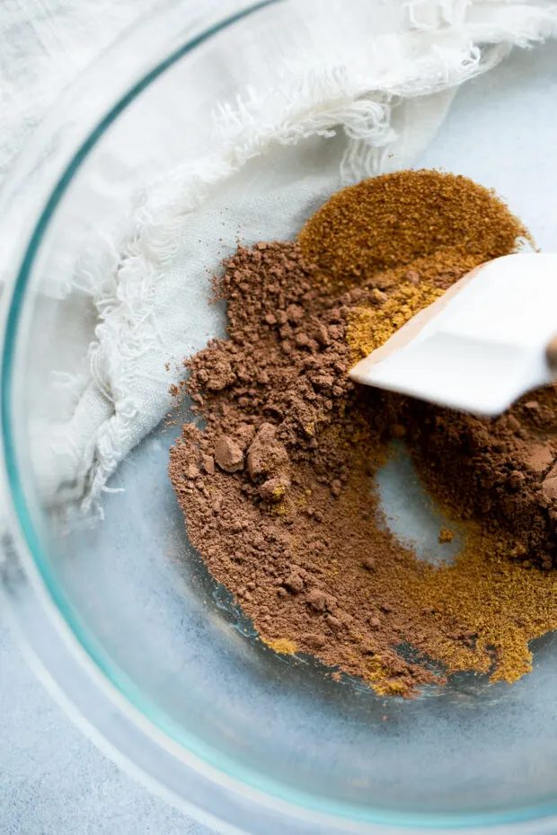 A clear glass bowl with cocoa powder, coconut sugar, and cayenne pepper.