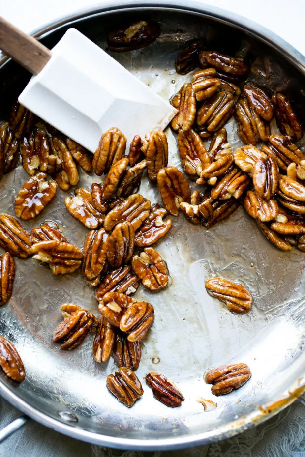 Maple glazed pecans in a skillet stirred by a white rubber spatula.
