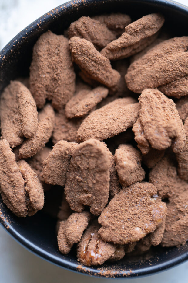 Finished candied pecans with cocoa-chili powder in a black serving bowl.