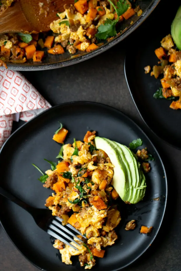 Sweet Potato Hash with Chorizo on black plates with sliced avocado on the side.