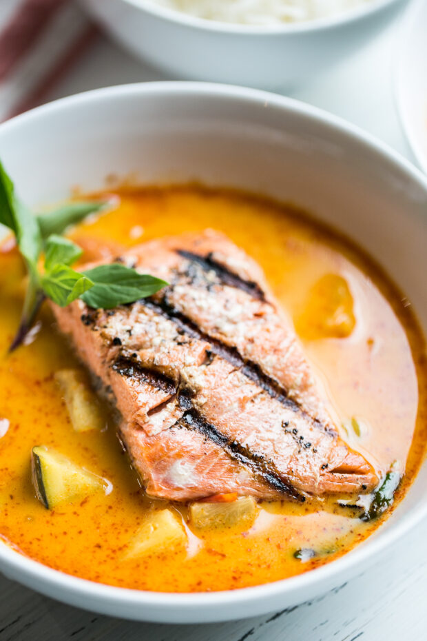 A bowl of Pineapple Curry with a grilled salmon fillet sitting on top. A sprig of Thai basil for garnish.