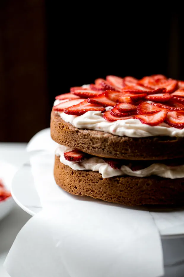 View of two cake layers from the side, each with a layer of frosting and strawberries.