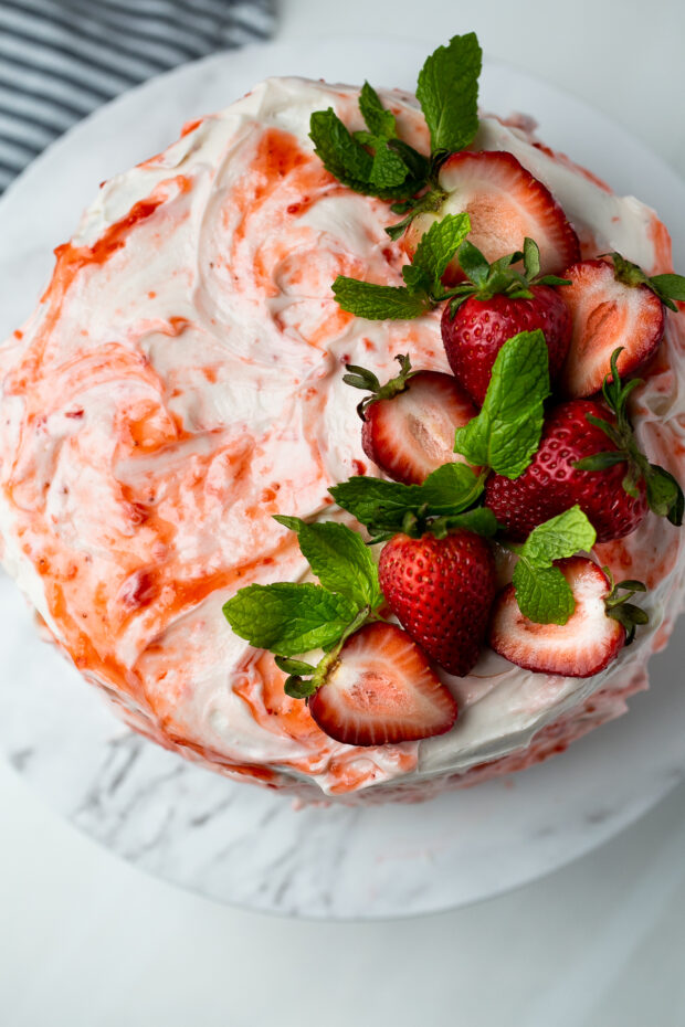View from the top of the vanilla layer cake with strawberry filling. Cake is swirled with strawberry jam and topped with fresh strawberries and mint leaves.