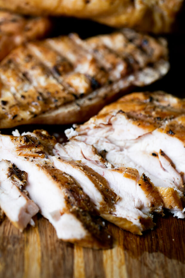 Smoked chicken breasts on a cutting board. One is sliced thinly.