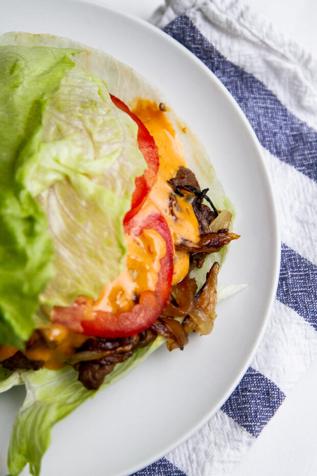 Caramelized Onion and Jalapeno Smash Burger with Chipotle Mayoand tomatoes in a lettuce bun on a white plate ready to eat.