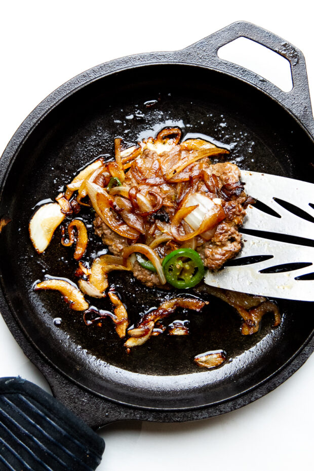 The smash burger patty has been flipped over revealing the deeply caramelized onions and jalapenos.