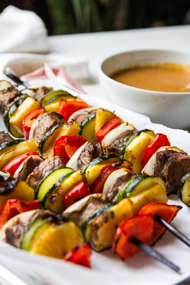 Freshly grilled Thai steak kebabs on a tray next to a bowl of Thai coconut curry sauce.