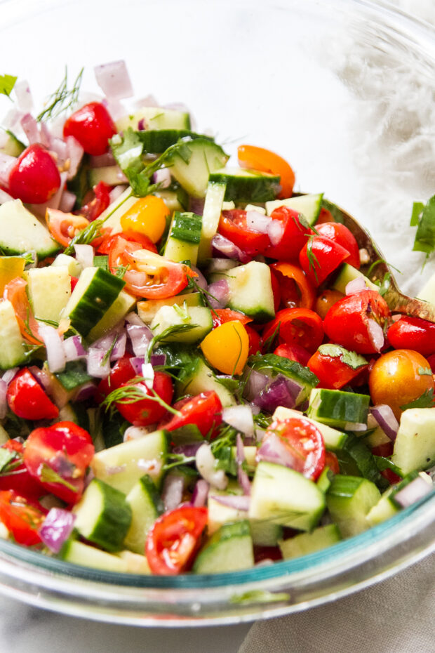 Mediterranean tomato cucumber salad without feta in a clear glass bowl.