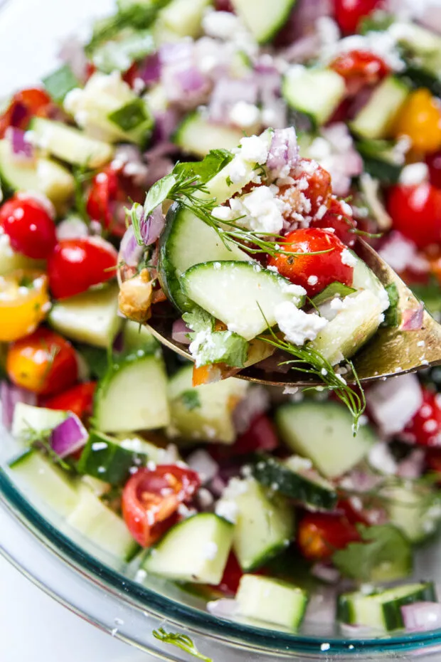 Finished salad with feta being scooped out of a large glass serving dish.