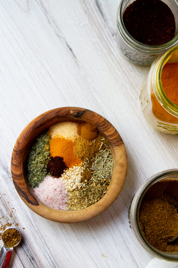 A small wooden bowl with the ingredients for the Middle Eastern Seasoning Blend. They have not been mixed together yet and the spices create a pretty mosaic in the bowl.