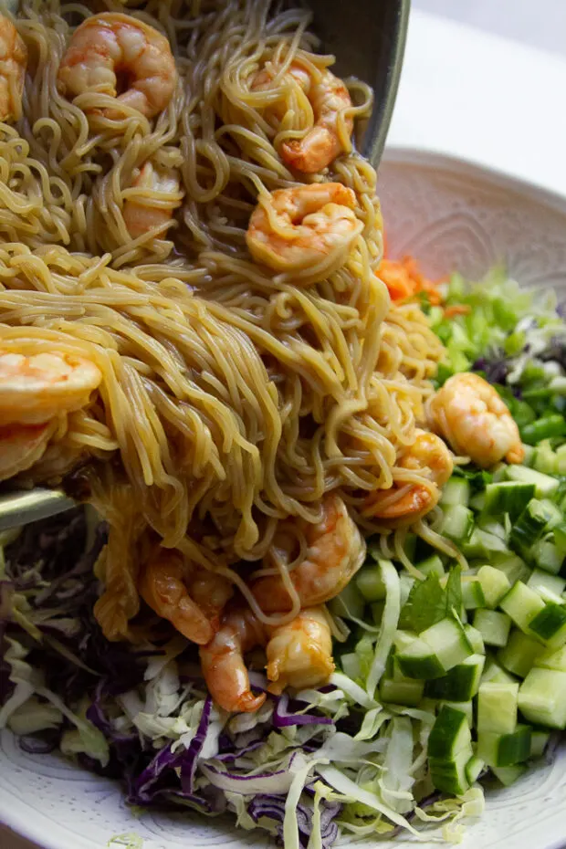 Cooked shrimp & rice ramen noodles coated in the Asian sauce are added to the raw vegetables in the large salad bowl.