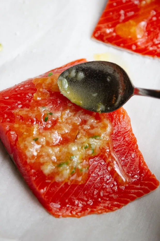 The garlic butter mixture is being spooned over the salmon fillets.