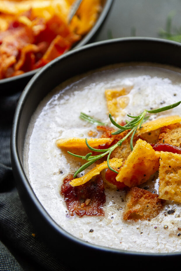 This dairy-free mushroom soup is in a black bowl with lots of garnishes including bacon & croutons.