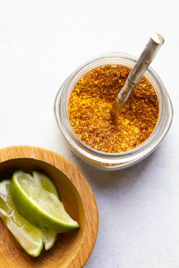 Glass spice jar with my Smoky Chipotle Taco Seasoning and a bowl of lime wedges.