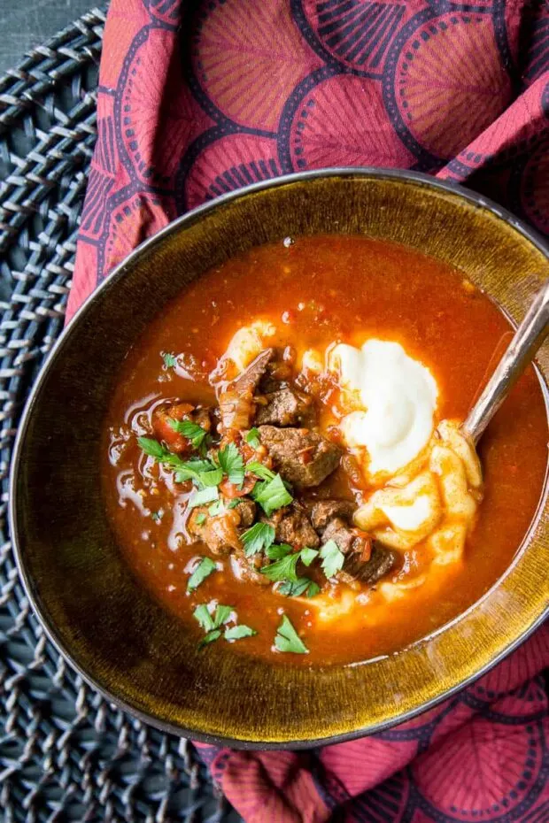 Top view of the styled bowl of Hungarian Goulash sitting on a burgundy napkin and a dark wicker charger.