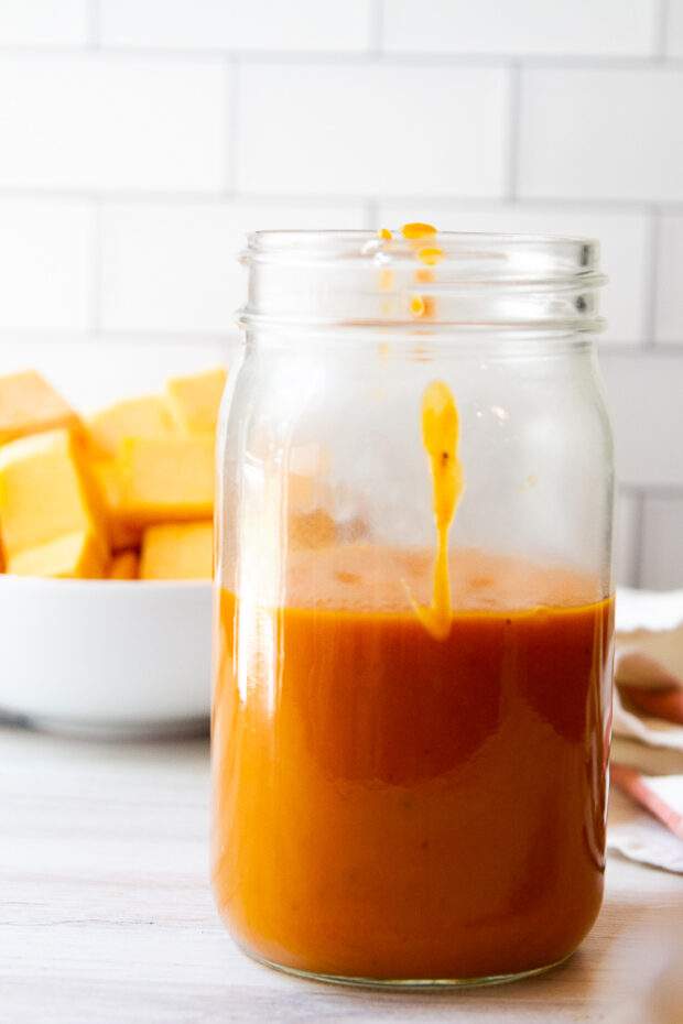 Another shot of the pasta sauce in a mason jar with a bowl of butternut squash cubes in the background