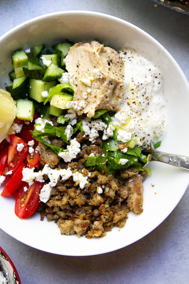 Mediterranean Ground Turkey Bowl in a white bowl topped with hummus, plain yogurt, cucumbers, tomato, and feta.