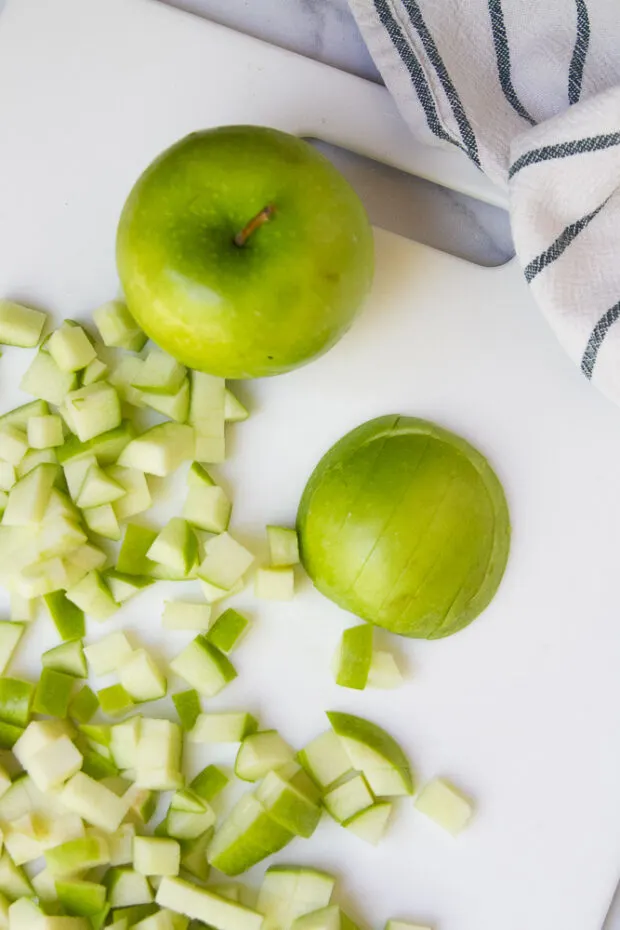A white cutting board with a green apple and another cut up green apple.
