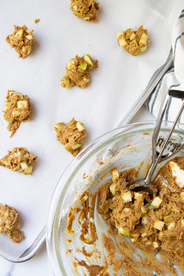 A parchment lined cookie sheet showing the cookie dough being scooped out. The dough is very apple heavy.