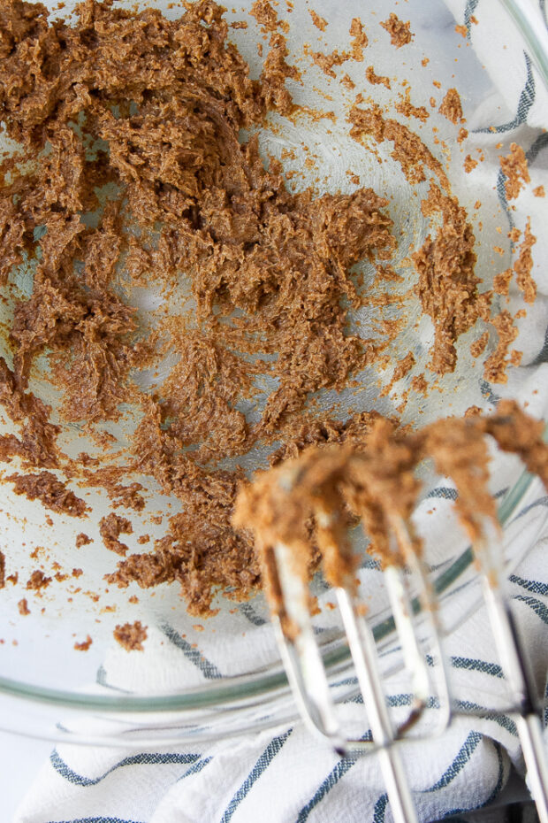 A big glass mixing bowl with coconut sugar and butter beaten with a hand mixer.