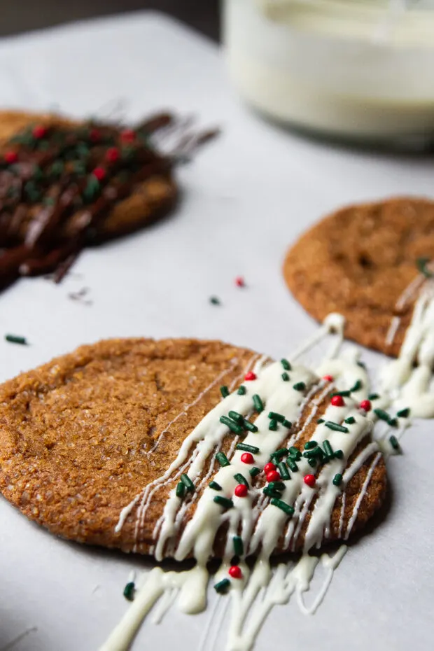 Close up of a ginger molasses cookie drizzled with white chocolate and sprinkled with red and green sprinkles.