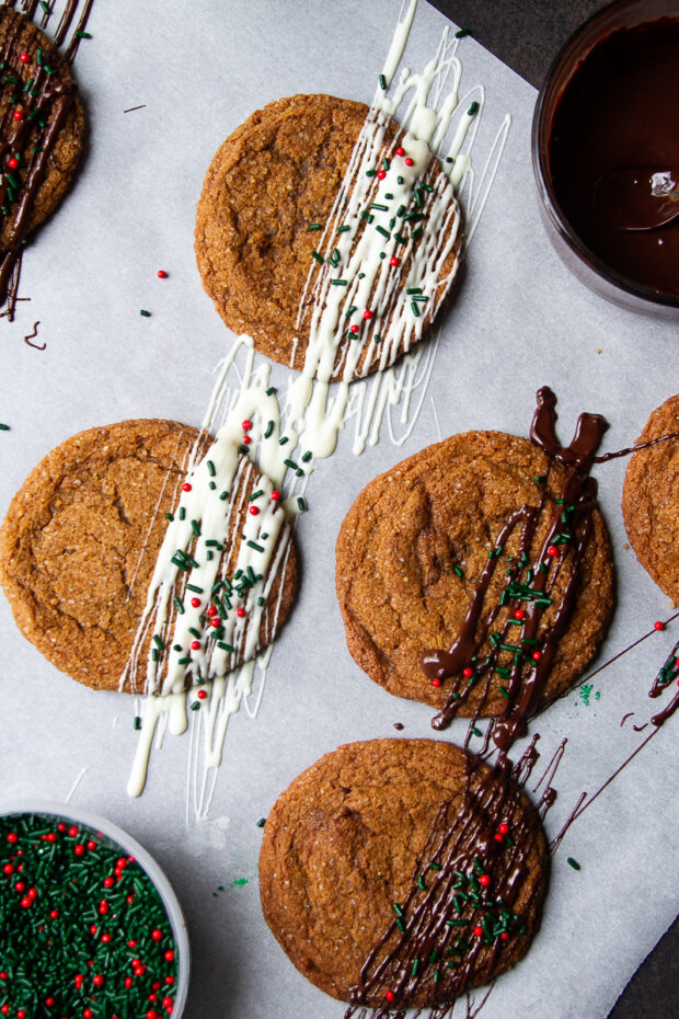 Baked gluten free ginger cookies on parchment. They're freshly drizzled -- some with white chocolate, some with dark chocolate and sprinkled with Christmas sprinkles.