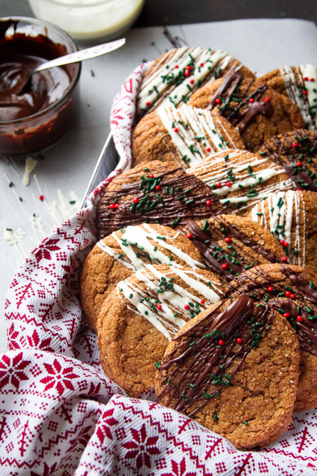 A towel lined tin filled with Gluten Free Ginger Cookies. Some are partially drizzled with white chocolate, some with dark chocolate, and they all have festive Christmas sprinkles.