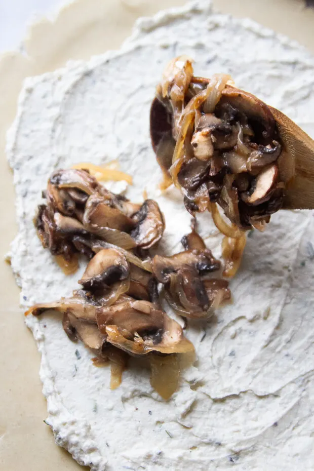 Spooning the caramelized onions and mushrooms over a rolled out pie crust topped with the ricotta filling.