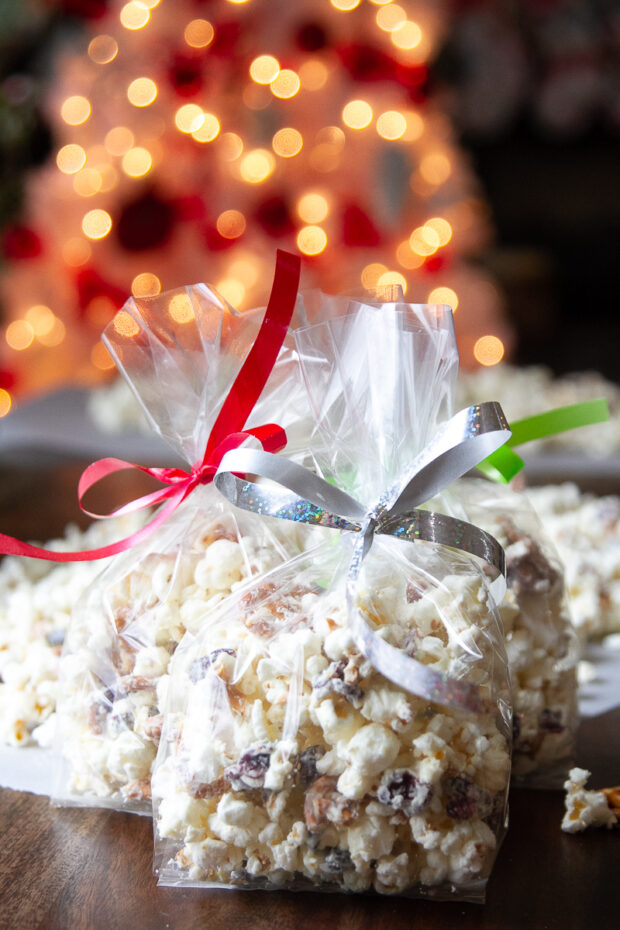 Bags of finished white chocolate popcorn in cellophane bags tied with Christmas ribbon.