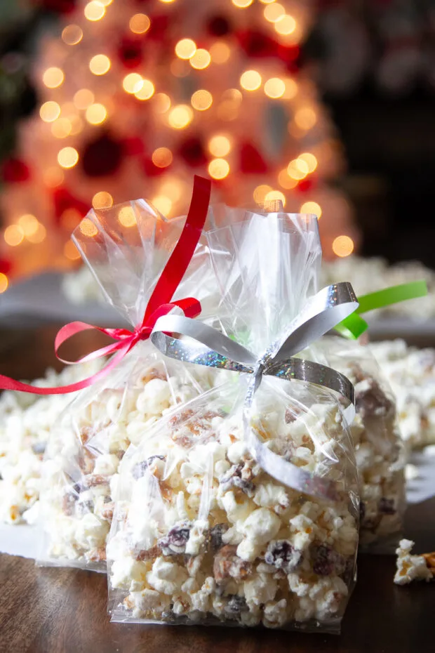 Bags of finished white chocolate popcorn in cellophane bags tied with Christmas ribbon.