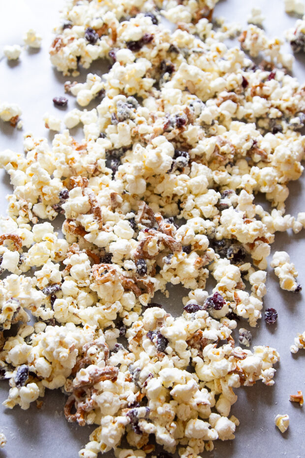 White chocolate popcorn with bits of cranberries and pretzels spread out on parchment waiting to set up.