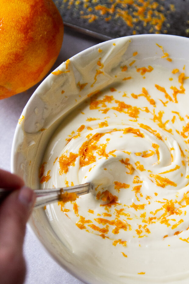 Orange zest being stirred into a bowl of melted white chocolate.