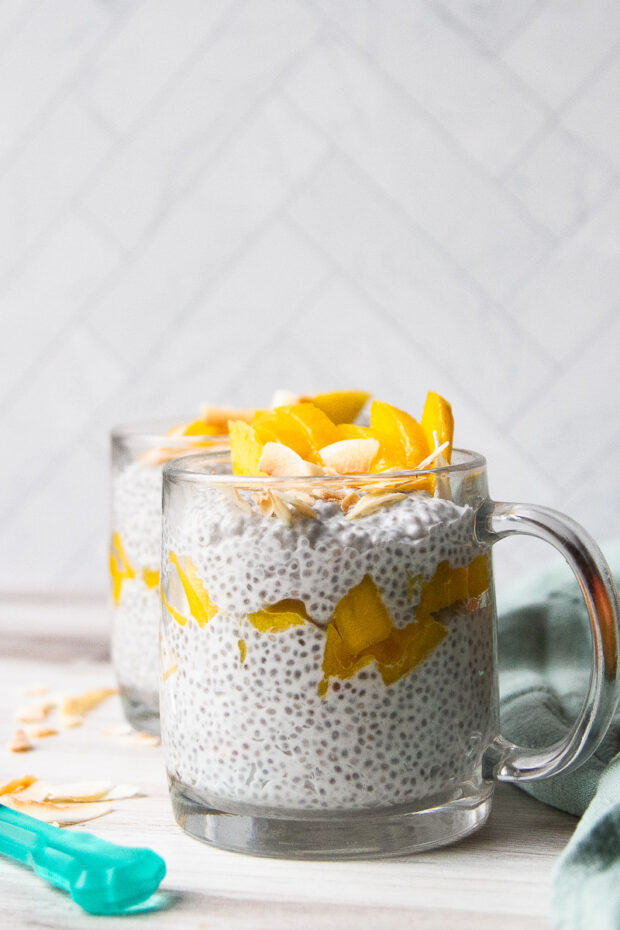 Clear mug filled with coconut chia seed pudding topped with sliced mango and toasted coconut flakes.