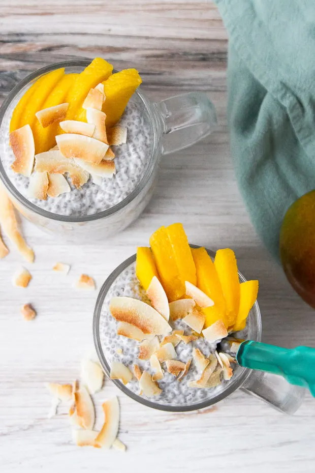 View from above -- two clear mugs with chia pudding topped with sliced mango and toasted coconut flakes ready to eat.