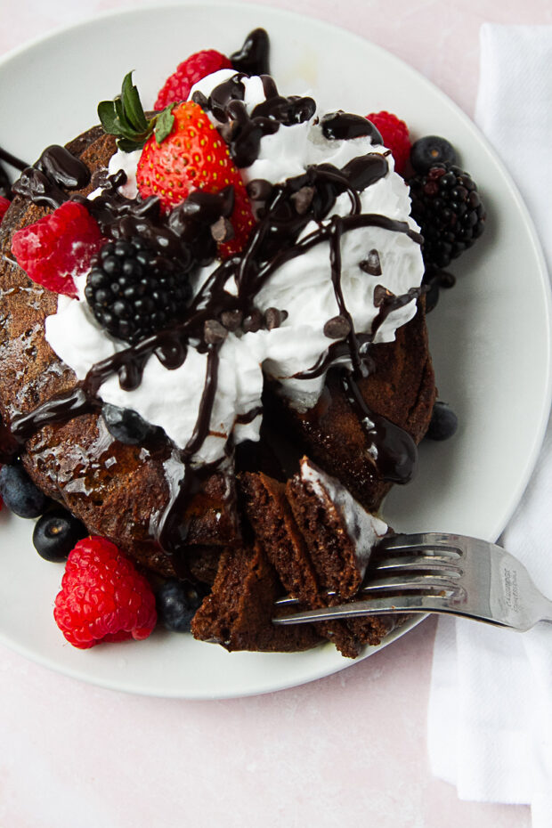 Pancakes are now drizzled with chocolate sauce and a section has been cut out with a fork.