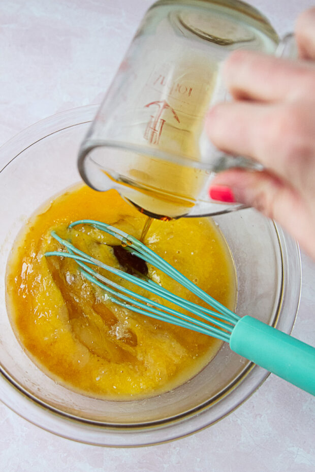 Maple syrup poured into a bowl with the other wet ingredients for paleo pancakes -- eggs, applesauce, vanilla extract, melted coconut oil.