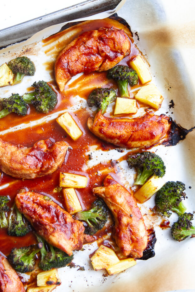 Parchment lined sheet pan with broiled BBQ chicken tenders, broccoli, & pineapple.