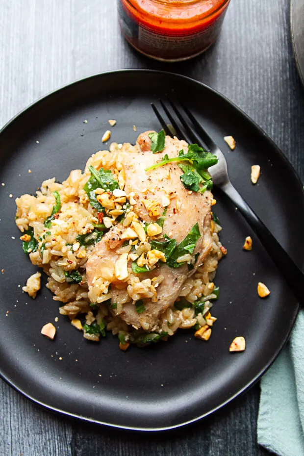 Chicken thigh and rice on a black plate with crushed peanuts.